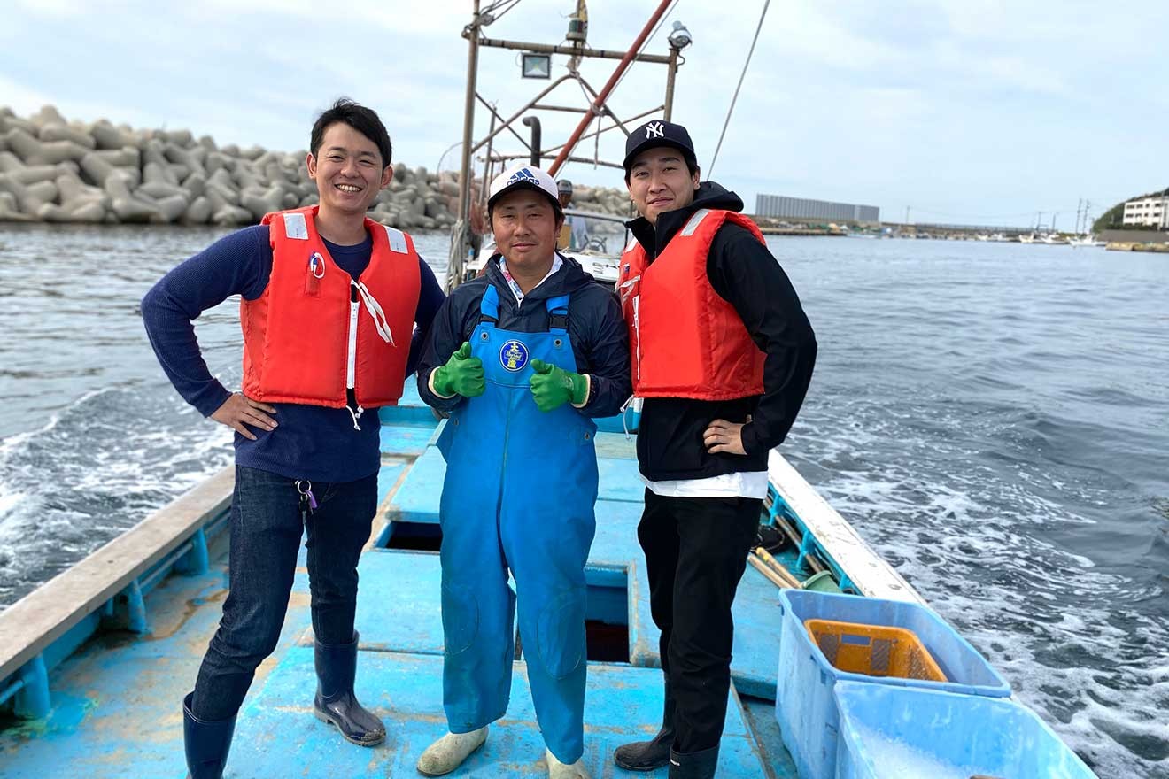 取引先の漁師(中央)と一緒に船上に立つ井口社長(左)。現場に足を運ぶことで、未利用魚だけではなく、様々な水産業界の情報を仕入れている(ベンナーズ提供)